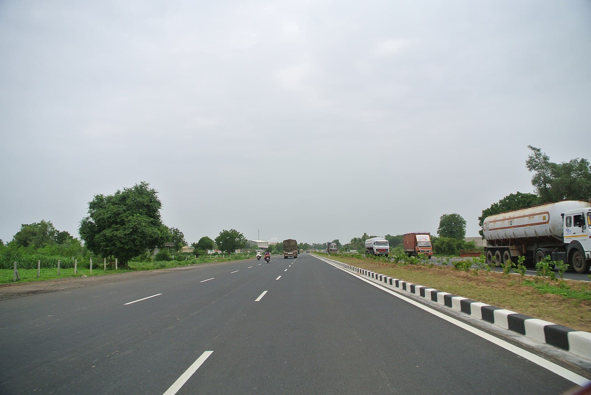 Freight trucks traveling on an open highway corridor beneath an overcast sky.